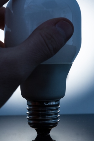 Hand holding an economic light bulb on reflective surfaceの写真素材