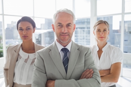 Confident businessman standing in front of colleagues with arms foldedの写真素材