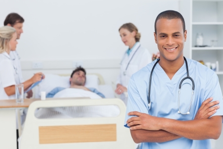 Attractive doctor with arms crossed standing in front of medical team taking care of a patientの写真素材