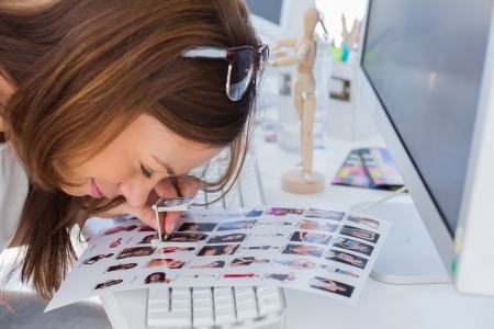 Editor using magnifying loupe to view contact sheet at her deskの写真素材