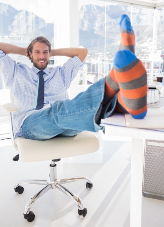 Shoeless designer kicking back at his desk and smilingの写真素材