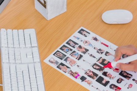 Close up of hand marking contact sheet on a desk with a keyboardの写真素材