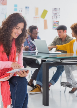 Smiling designer using tablet pc while others are at work behindの写真素材
