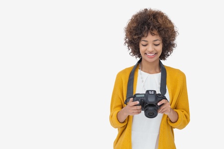 Woman looking at her digital camera and smiling on white background