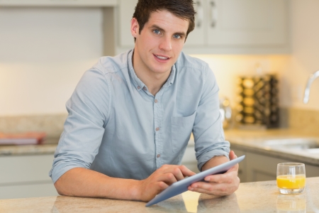 Man with tablet pc and orange juice in kitchenの写真素材