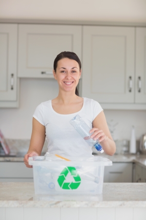 Smiling woman throwing bottle into recycling bin in kitchenの写真素材