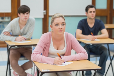 Three students sitting at desks in a classroom listening and about to take notesの写真素材