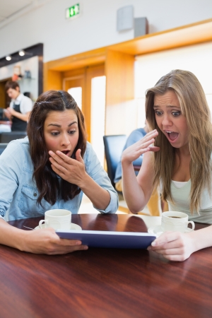 Women looking surprised while holding a tablet in the canteenの写真素材