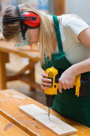 Student using the drill while standing in a woodworking class and drilling a holeの写真素材