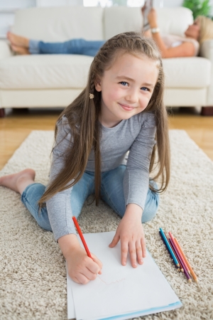 Happy girl drawing with her mother reading newspaper on the couch in the living roomの写真素材