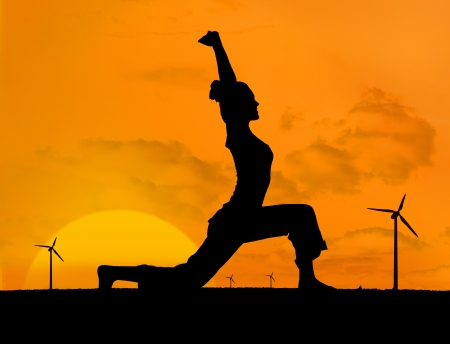 Silhouette of woman doing yoga with wind turbines on the background under sunsetの写真素材
