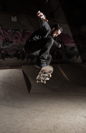 Skater doing huge ollie in the skate park with ramp behind himの写真素材