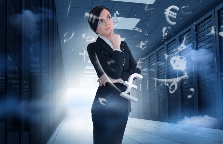 Businesswoman standing and thinking in data center with currency graphicsの写真素材
