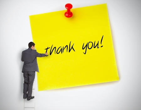 Businessman writing thank you on a giant post it on white backgroundの写真素材