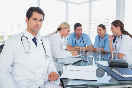 Doctor smiling to the camera while his team worksの写真素材