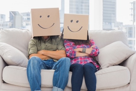 Funny workers with arms crossed wearing boxes on their heads with smiley faces on a couchの写真素材