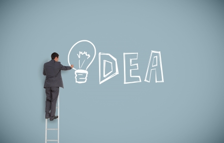 Buisnessman on ladder writing idea with light bulb as the i on grey wallの写真素材