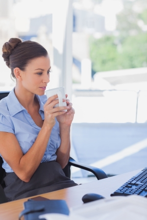 Businesswoman holding her mug and looking at her computer in the officeの写真素材
