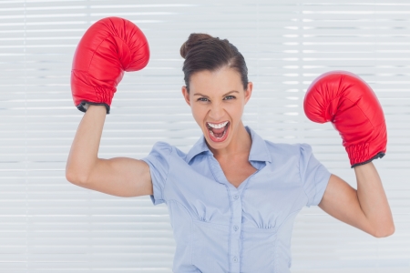Businesswoman in boxing gloves cheering in the officeの写真素材