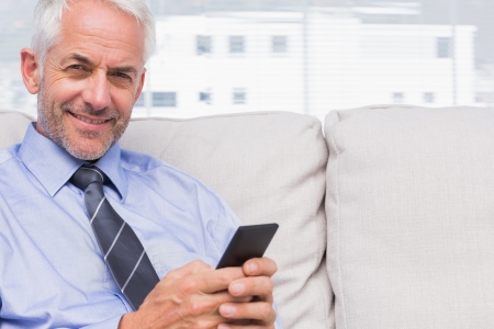 Happy businessman using smartphone on couch in staffroomの写真素材