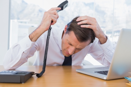 Annoyed businessman holding the telephone in his officeの写真素材