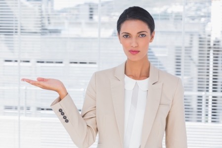 Pretty businesswoman opening her hand in a bright officeの写真素材
