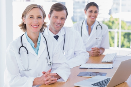 Cheerful doctors posing at their desk with a laptop computerの写真素材