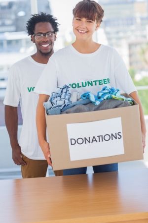 Cheerful woman holding donation box full of clothes with a colleague next to herの写真素材
