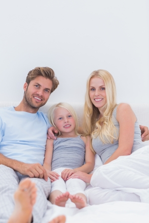 Beautiful family sitting in bed and looking at cameraの写真素材