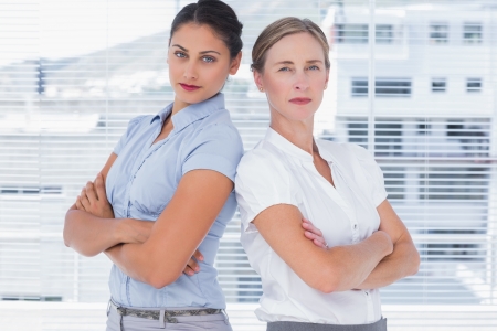 Stern businesswomen standing back to back with arms crossedの写真素材