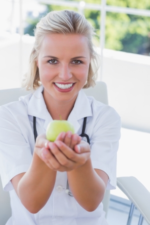 Pretty blonde nurse holding a green appleの写真素材