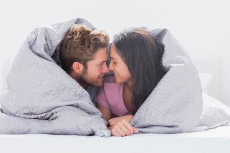 Couple wrapped in the duvet in bedの写真素材