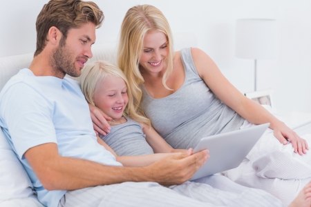 Couple using a laptop with their daughter in bedの写真素材