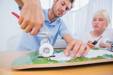Father repairing a skateboard with his son in the living room
