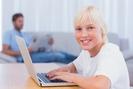 Little boy using laptop while his father is reading on the couch in the living roomの写真素材