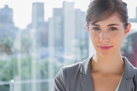 Pretty businesswoman smiling at camera beside large windowの写真素材