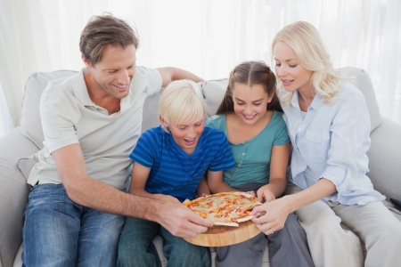 Family eating pizza together sitting on a couchの写真素材
