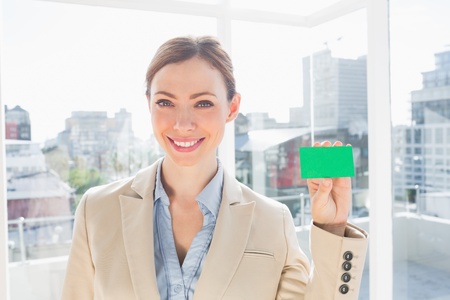 Smiling businesswoman showing green business card by large windowsの写真素材