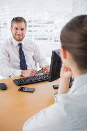 Businessman smiling at camera at his desk with co workerの写真素材