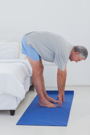 Mature man stretching on an aerobic mat in his bedroomの写真素材