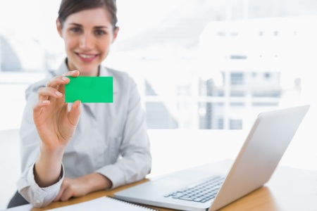 Young businesswoman showing green business card at her desk in officeの写真素材