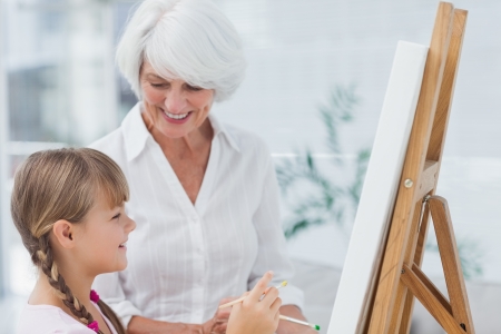 Grandmother and cute granddaughter painting together at homeの写真素材