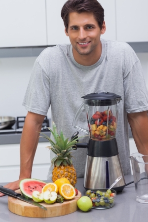 Handsome man leaning on the counter of his kitchen with several fruitsの写真素材