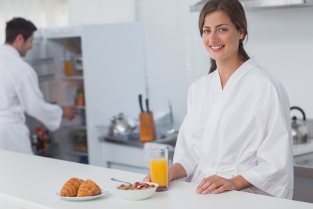 Woman having breakfast with cereal and orange juice with croissants with her husband on the backgroundの写真素材