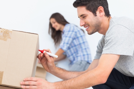 Happy man writing with a red marker on a moving boxの写真素材
