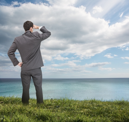 Stylish businessman standing on the grass and looking at the sea Stylish businessman standing on the grass and looking at the sea