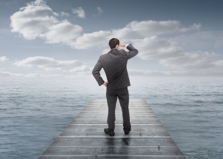 Businessman standing on a bridge and looking at the seaの写真素材