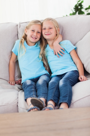 Cute twins sitting on a couch in the living roomの写真素材