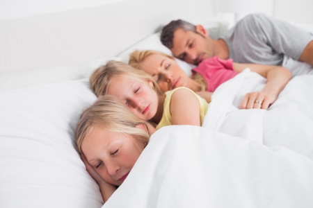 Parents sleeping with their cute children in bedの写真素材