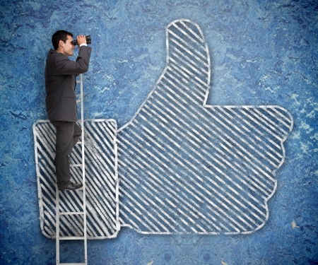 Businessman on a ladder with a thumb up of the social network behind  の写真素材